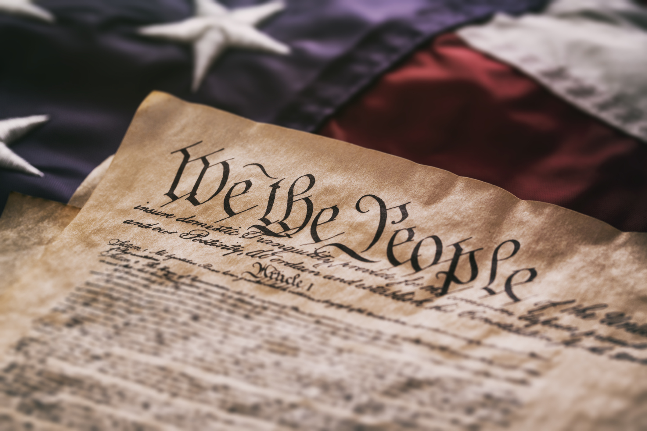 We The People - An old USA Constitution on parchment paper lying on a old American flag.